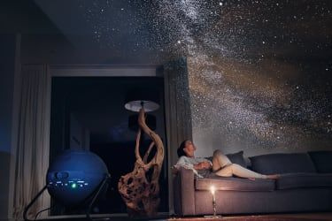 Kvinde sad på sofaen og kiggede på projektion af stjerner på loftet