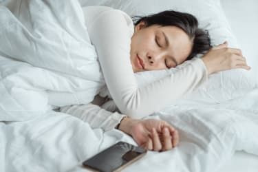 Ženska spi v postelji s pametnim telefonom ob sebi