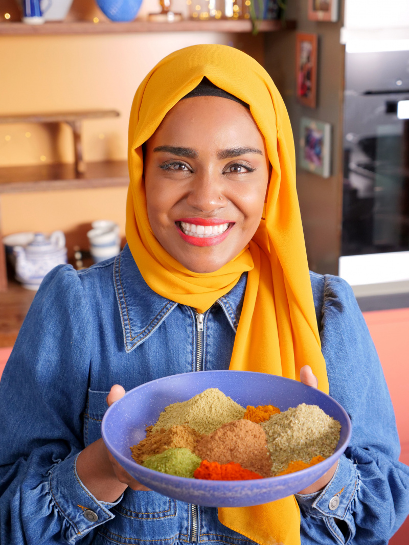   Nadiya Hussain houdt een kom vol kleurrijke kruiden vast.