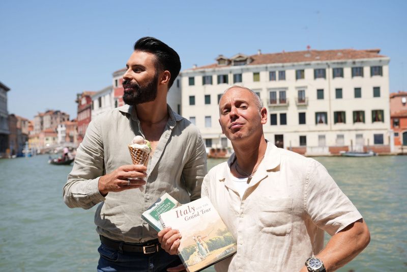   Rylan ถือไอศกรีมและ Rob ถือหนังสือ Grand Tour สองเล่มขณะที่พวกเขายืนอยู่หน้า Grand Canal