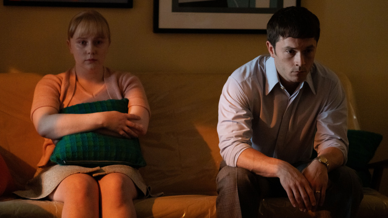   júna's parents sit side by side on the sofa looking sad