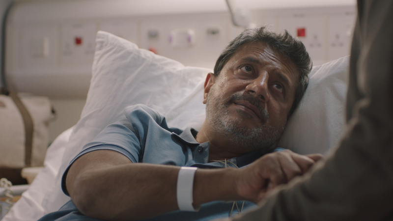   Ravin J. Ganatra als Kareem in een ziekenhuisbed met uitslag's hand.