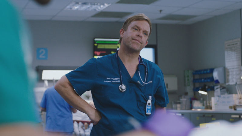   Dylan Keogh, Casualty'de klasik elini kalçasına koyarak poz veriyor.