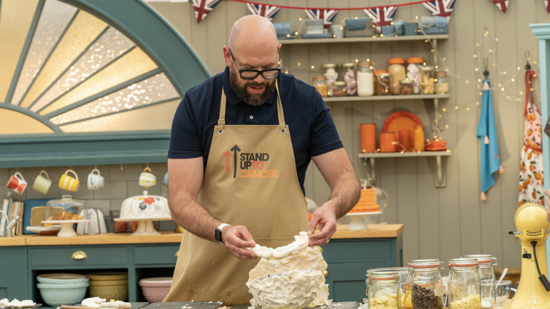   Том Дейвис в тъмно горнище и бледа престилка прави меренг в The Great Celebrity Bake Off за Stand Up to Cancer