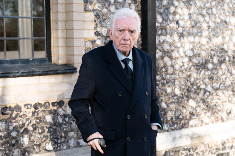  Alan Ford als Stevie Mitchell in EastEnders. Hij draagt ​​een zwart pak en houdt een wandelstok vast.