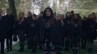 Eine Gruppe von Cheerleadern in trauernden Cheerleader-Kostümen, angeführt von Cheryl Blossom, sieht bei einer Beerdigung emotional aus