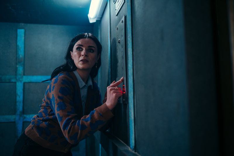 Sarah (Aisling Bea) stoi w windzie gorączkowo naciskając przyciski, z wyrazem niepokoju na twarzy