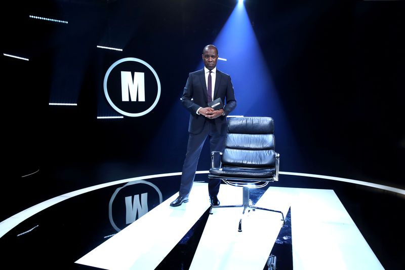 Ο Clive Myrie στέκεται στο στούντιο Mastermind δίπλα στους διαγωνιζόμενους
