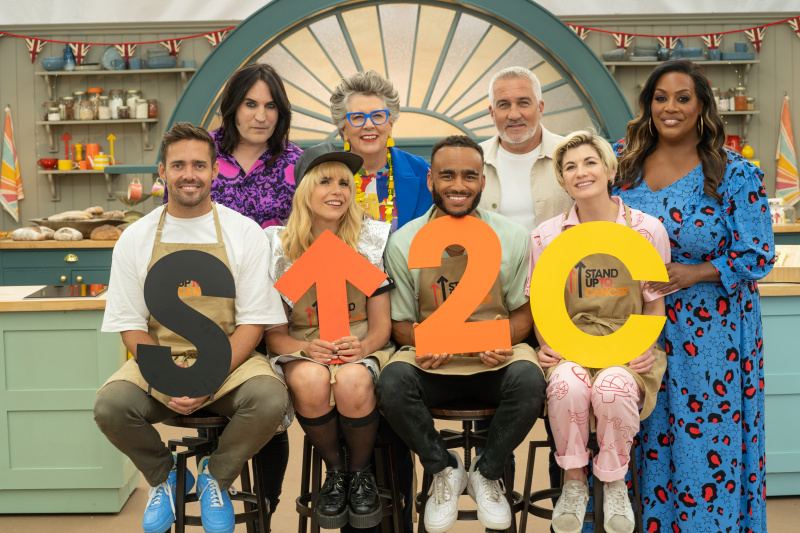   Noel Fielding, Prue Leith, Paul Hollywood in Alison Hammond stojijo za Spencerjem Matthewsom, Palomo Faith, Munyo Chawawa in Jodie Whittaker, ki držijo logotip Stand Up to Cancer v šotoru za The Great Celebrity Bake Off for Stand Up to Cancer.