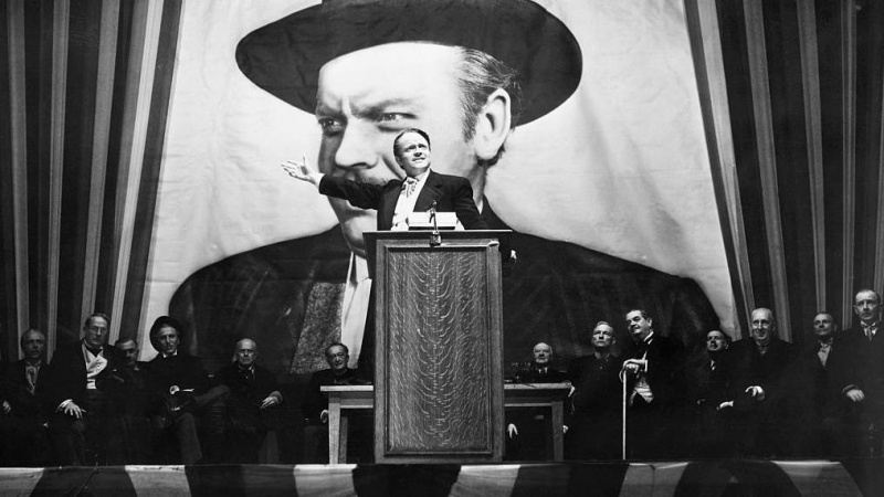   harles Foster Kane (Orson Welles) prednáša strhujúci prejav pred kampaňou pred portrétom seba samého, ktorý je väčší ako život v scéne z filmu Občan Kane.