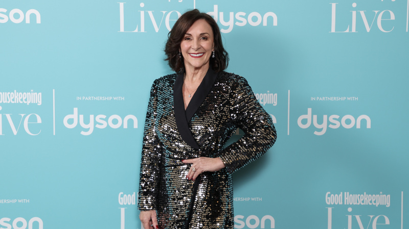   Shirley Ballas สวมชุดที่แวววาวตัดกับพื้นหลังสีเขียว