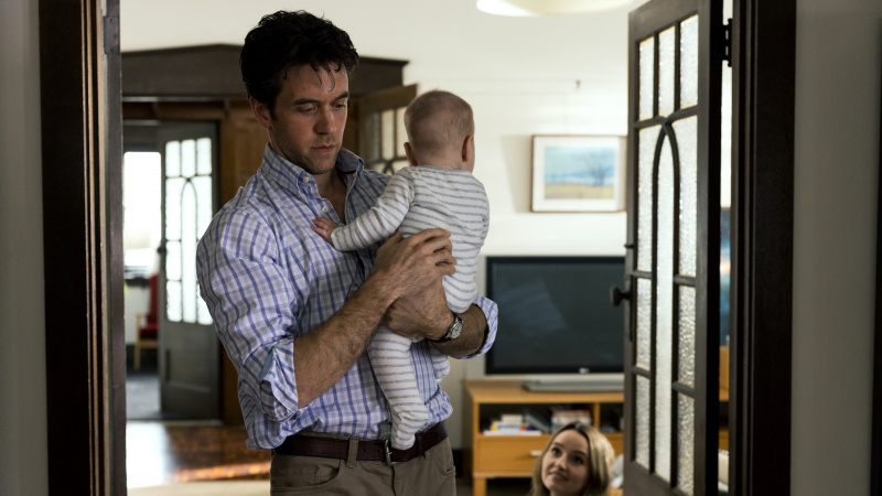   ベルとしてのアシュリー・ズカーマン's partner Clive, looking downcast and holding her baby son, while she looks on.