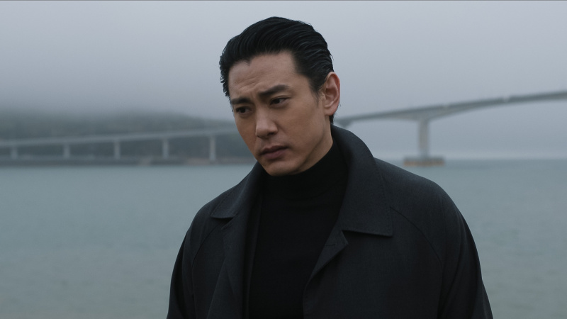   Jang stă lângă apă's edge with a bridge behind him in The Recruit season 2