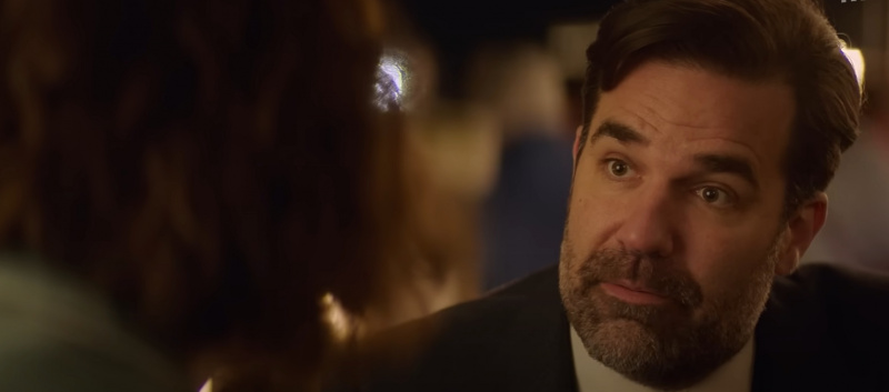   Andrew Sullivan draagt ​​een pak en praat met Hadley.