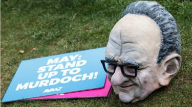 En dukkehoved af Rupert Murdoch sidder ved siden af et anti-overtagelsesskilt uden for parlamentet