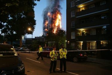 TOPSHOT - Politiet bemander en sikkerhedsafspærring, da en enorm brand opsluger Grenfell Tower i begyndelsen af den 14. juni 2017 i det vestlige London. Den massive brand slog igennem den 27-etagers boligblok i det vestlige Lond