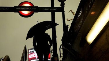 Un bărbat ține o umbrelă în fața stației de metrou din Londra