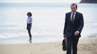 Ο Richard Poole σε μια παραλία στο Death in Paradise με φόντο την Camille