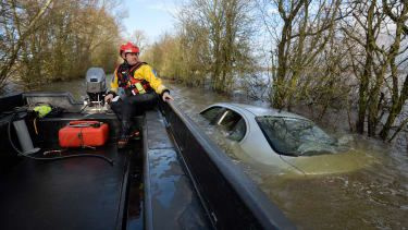 Um policial em um barco olha para um carro submerso na berma de uma estrada inundada que leva ao vilarejo isolado de Muchelney em Somerset, sudoeste da Inglaterra, em 26 de janeiro de 2014. Um conselho local