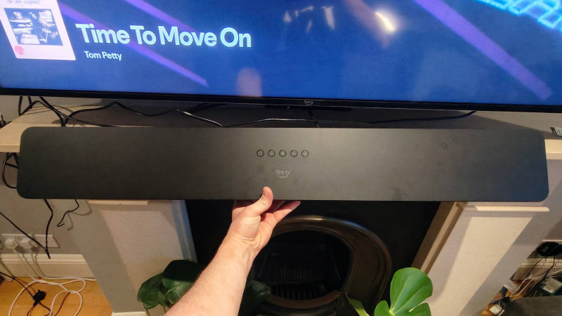   Amazon Fire TV Soundbar Plus pod Amazon TV, v mužovi's hand.