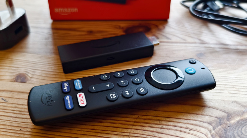  Amazon Fire TV Stick vedľa diaľkového ovládača a krabice na drevenom stole.
