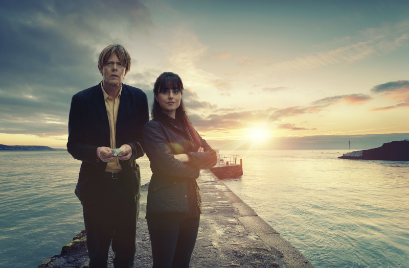 Beyond Paradise ซีซั่น 2 ตัวละคร DI Humphrey Goodman (Kris Marshall) และ DS Esther Williams (Zahra Ahmadi) ยืนอยู่หน้ามหาสมุทรในท่าโพสท่า โดยมีพระอาทิตย์ตกเหนือเขื่อนกันคลื่นด้านหลัง