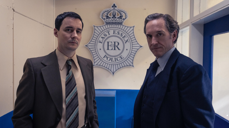   クライヴ・ロスコー刑事役のサム・スウェインズベリーとダルグリーシュ役のバーティ・カーベルがダルグリーシュのイーストエセックス警察の標識の前に立つ。