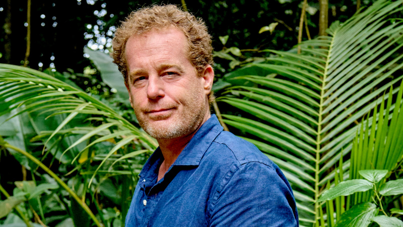   Rick (Adam James), okyanus mavisi pamuklu bir gömlek giyen bazı palmiye cephelerinin önünde duruyor