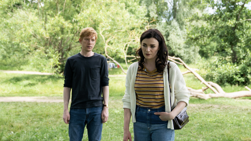   Jack ve Aisling Bea çizgili üst, beyaz hırka ve kot pantolonla Domhnall Gleeson koyu renkli bir üst ve kot pantolonla Lynn, Alice & Jack'teki ormanlık bir alanda birlikte dururken