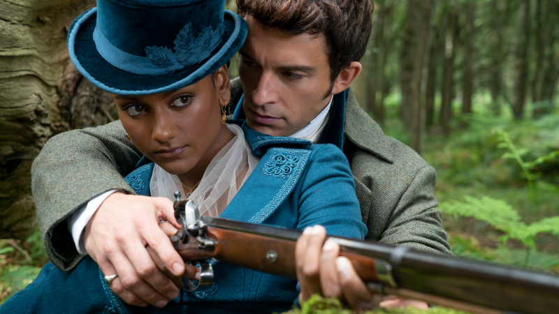   Kate Sharma (Simone Ashley) y Anthony Bridgerton (Jonathan Bailey) se abrazan mientras Anthony le enseña a Kate cómo usar un rifle.