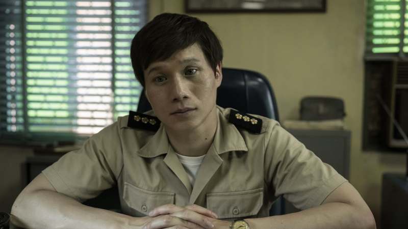   Hoa Xuande în uniformă, în timp ce căpitanul stă la un birou în The Sympathizer.