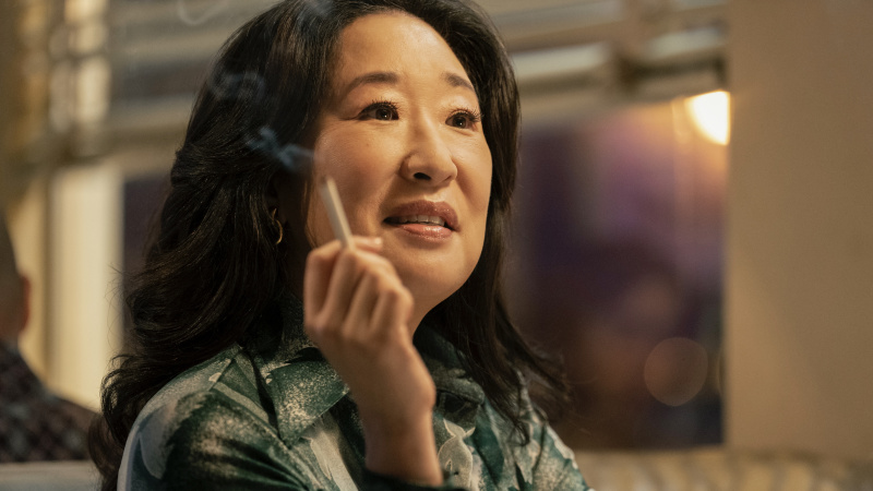   Sandra Oh într-un top verde ținând o țigară ca Sofia Mori în The Sympathizer.