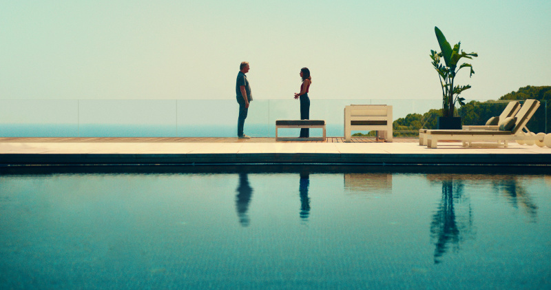   Daniel Lang (Douglas Henshall) og Erin Carter (Evin Ahmad) står overfor hverandre på den andre siden av et strålende blått svømmebasseng, med havet synlig bak en lav glassvegg bak dem