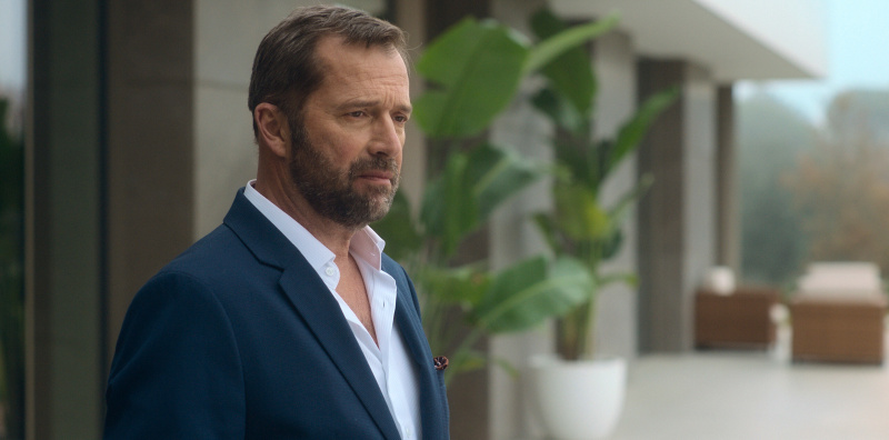   Fred (James Purefoy) steht im Anzug und mit nachdenklicher Miene auf dem Gelände eines schick aussehenden Hauses, das zwar sichtbar, aber unscharf hinter ihm ist