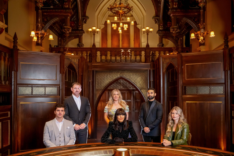   Claudia Winkleman est assise à la table ronde dans le château des Traîtres avec les finalistes de la série 2, qui sont tous habillés de manière élégante et formelle. Assis à la table à gauche de la photo se trouve Harry Clark, avec Andrew Jenkins debout derrière lui. Evie Morrison se tient derrière Claudia et Jaz Singh se tient à côté d'elle. Mollie Pearce est assise à la table à droite de la photo.