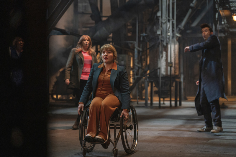   Shirley Anne Bingham (Ruth Madeley), tekerlekli sandalyesini silahları ateşlemeye hazır bir şekilde kapının önüne yerleştirirken, Sylvia (Jacqueline King), Donna (Catherine Tate) ve Doktor (David Tennant) geride duruyor.