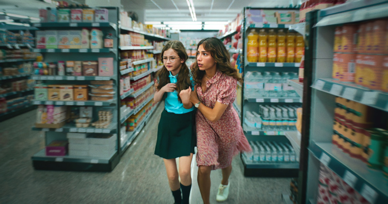  ภาพนิ่งจาก Who Is Erin Carter? แสดงให้เห็น Erin (Evin Ahmad) กอดลูกสาว Harper's (Indica Watson) shoulders. They are both slightly hunched forwards and the shelves around them are out of focus, implying that they are moving quickly
