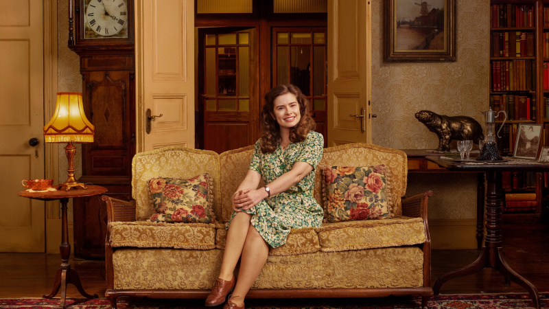 Rachel Shenton v zelených kvetinových šatách ako Helen sedí na pohovke v Skeldale House v All Creatures Great and Small
