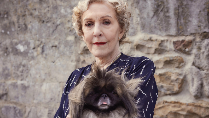   Patricia Hodge v tmavých šatách ako pani Pumphrey drží pekinského Tricki Woo vo filme All Creatures Great and Small.