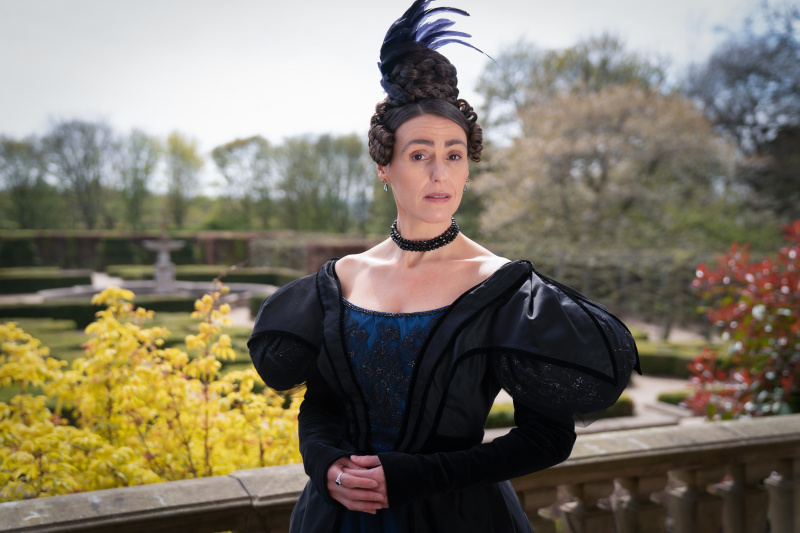   Suranne Jones kao Anne Lister u Gentlemanu Jacku stoji na terasi u tamnoplavoj haljini s perom u kosi.