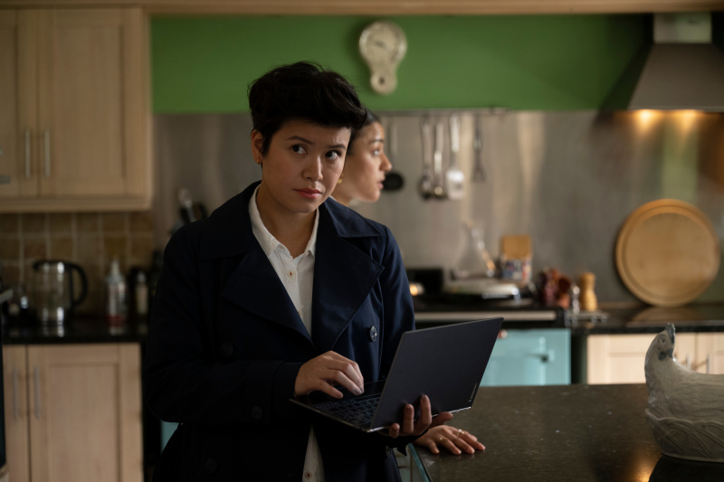   DC Blair Ferguson (Katie Leung) ยืนอยู่ในครัว กำลังพิมพ์บนคอมพิวเตอร์แล็ปท็อปที่เธอ's holding with her other hand