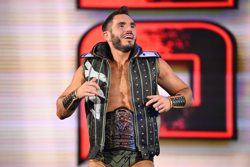   Johnny Gargano se prebija v ring, oblečen v usnjeno jakno brez rokavov, z usnjenimi manšetami in usnjenim pasom za naslov WWE