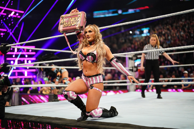   Tiffany Stratton kleči na robu obroča, zunaj vrvi, in drži roza in zlato"Money In The Bank" briefcase to show the crowd