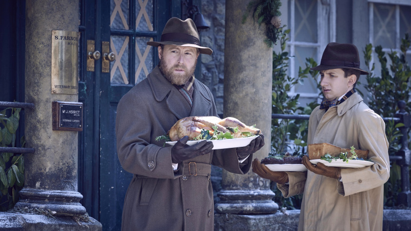  Samuel West en James Anthony-Rose met hoeden en jassen terwijl Siegfried en Carmody in de sneeuw staan ​​met voedsel in All Creatures Great and Small.