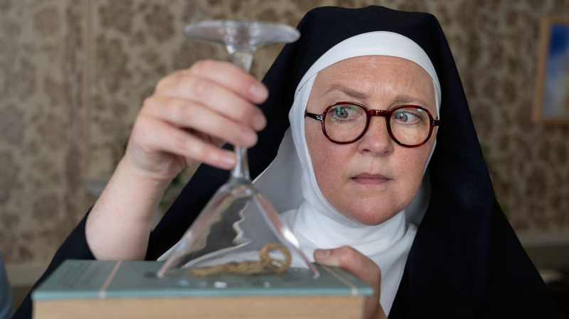   Sœur Boniface (Lorna Watson) tenant un piège à scorpion sous un verre à martini dans la saison 3 de Sister Boniface Mysteries