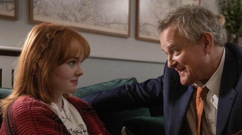   Claudia kanepede otururken kırmızı hırkalı Madeleine Power, Douglas İptal Edildi'de Douglas elini tutarken Hugh Bonneville takım elbiseli.