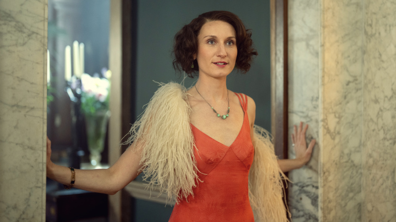   Bessie Carter punases kleidis ja valge suleboaga Nancy Mitfordina filmis Outrageous