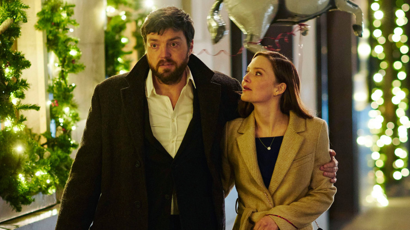  Strike: The Ink Black Heart Cormoran Strike (Tom Burke); Robin Ellacott (Holliday Grainger) merge cu brațul în jurul ei.