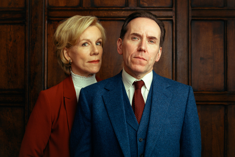  Dr. Helena Goldberg (Juliet Stevenson) steht hinter der rechten Schulter von Professor Jasper Tempest (Ben Miller) in einem mit Mahagoni getäfelten Raum. Sie hat den Hauch eines Lächelns, er sieht völlig ernst aus.