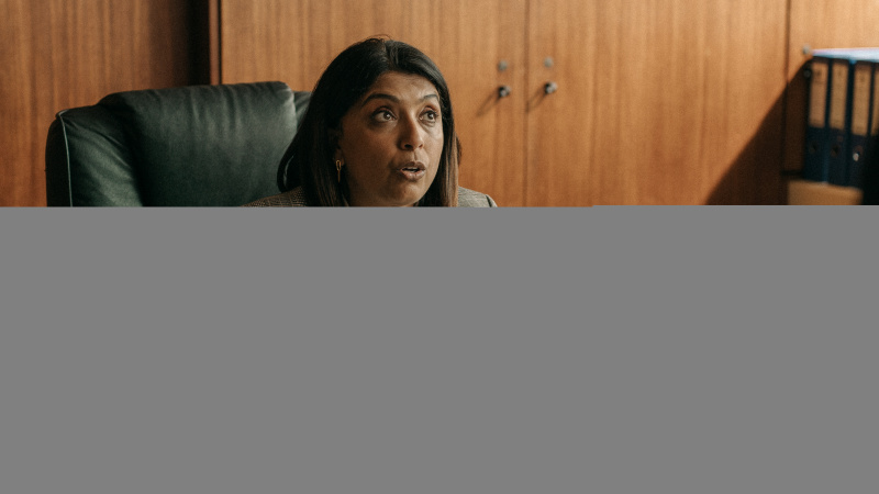  DCI Maiya Goswami (Sunetra Sarker) sitzt in einem Ledersessel mit hoher Rückenlehne an ihrem Schreibtisch und hebt in einer Art Protestgeste die Hände